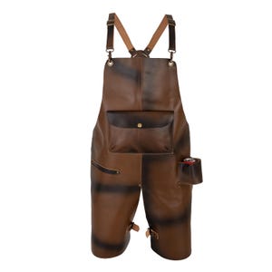 May include: A brown leather apron with adjustable straps and multiple pockets. The apron features a chest pocket with a button closure and a side pocket. The leather has a distressed appearance with darker brown accents.