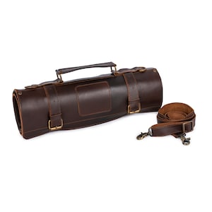 May include: A brown leather knife roll with a strap and buckle closures. The roll has a handle and is rolled up.