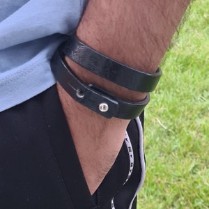 May include: A black leather bracelet with a silver buckle. The bracelet is worn on a person's wrist.
