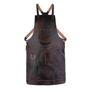 May include: A dark brown leather apron with two front pockets and a chest pocket. The apron has adjustable straps and a metal ring on the front. The apron is designed for use in a kitchen or workshop.