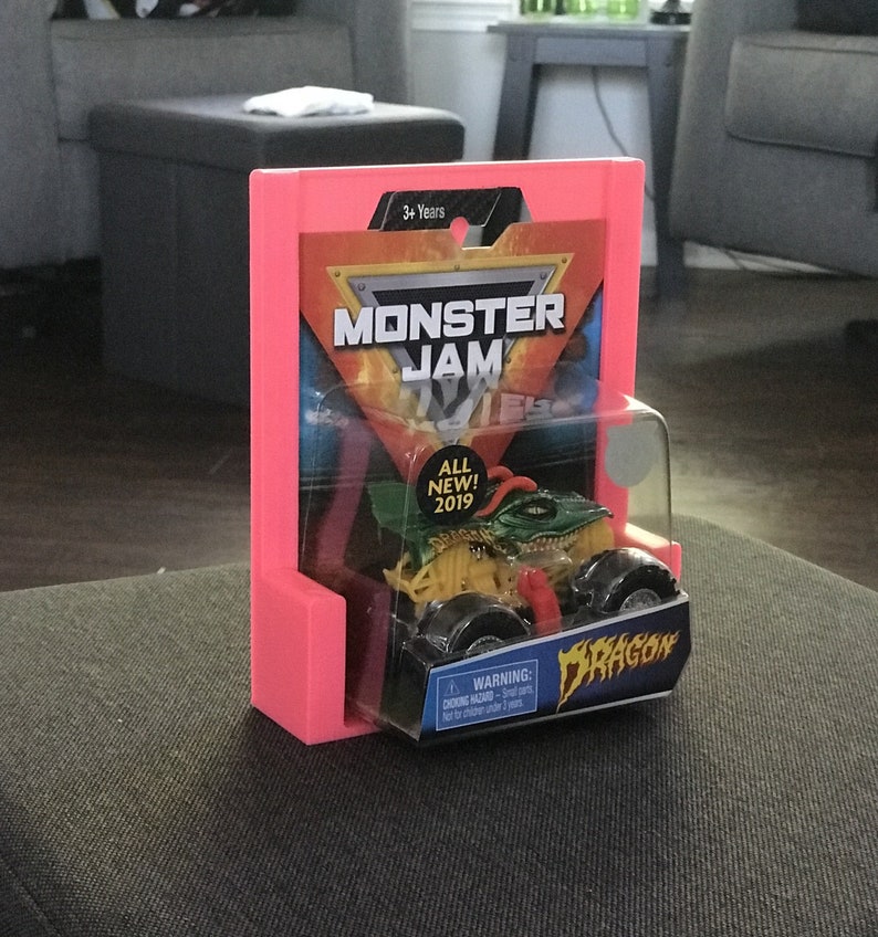 Puede incluir: Un expositor de pl&aacute;stico rosa con un cami&oacute;n de juguete Monster Jam en su interior. El cami&oacute;n es verde, amarillo y negro con un dise&ntilde;o de drag&oacute;n. El embalaje dice "Monster Jam" y "&iexcl;Nuevo! 2019".
