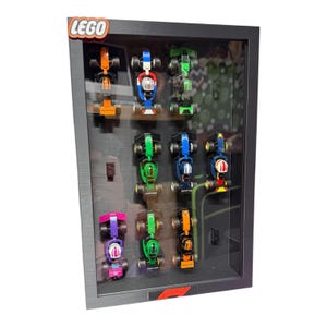 May include: A black framed display case with multiple colorful Lego race cars. The Lego logo is in the top left corner. The cars are in various colors including orange, green, blue, and pink. The display case has a glass front.