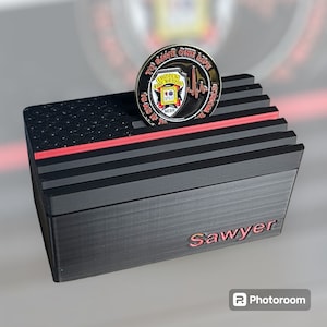 May include: Black wooden box with a red stripe and the word "Sawyer" engraved on the front. A gold coin with the words "To Save One Life Is As If It's The Whole World" and a fire department logo is on top of the box.
