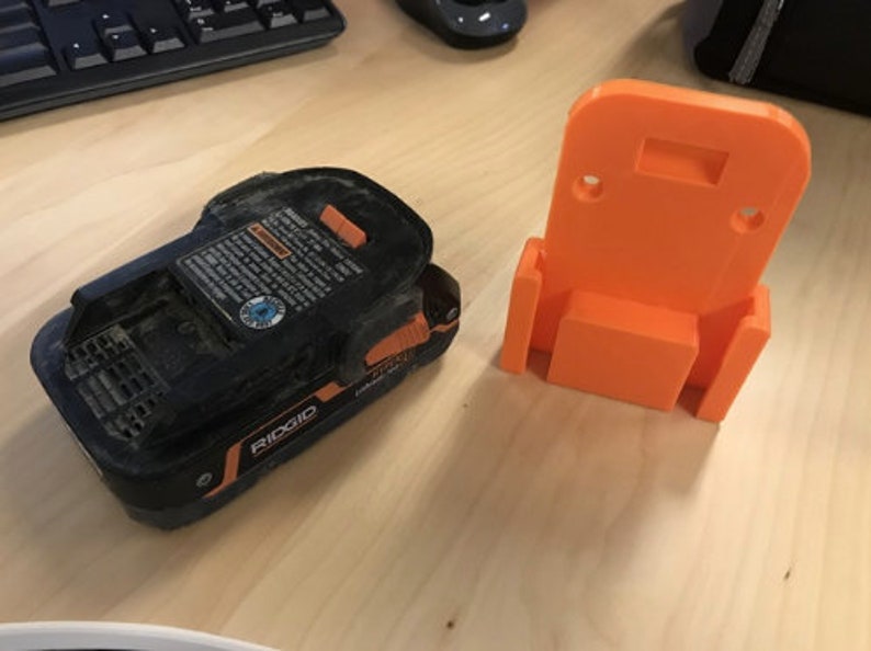May include: A black and orange power tool battery with a warning label and the word "RIDGID" printed on it. A bright orange plastic wall mount for the battery is also shown.