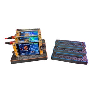 May include: A stack of three small electronic devices with screens displaying data, connected by red and black wires. The devices are mounted on a black and orange base. To the right, there is a stack of three black and blue platforms.