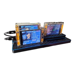 May include: A black and blue electronic device with multiple screens displaying data. The screens are encased in clear plastic and mounted on a black base. A USB cable is connected to the device. The screens show numbers and graphics.