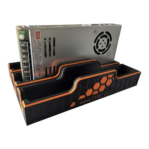 May include: A silver-colored power supply unit is mounted in a black and orange holder. The holder has a honeycomb pattern and the text "www.TTRC.us" on the front. The power supply has a fan and various ports.