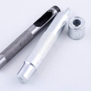May include: A set of three silver metal tools for punching holes in leather. The tools include a punch, a hammer, and a setting tool.