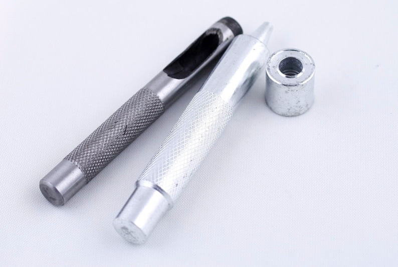May include: A set of three silver metal tools for punching holes in leather. The tools include a punch, a hammer, and a setting tool.