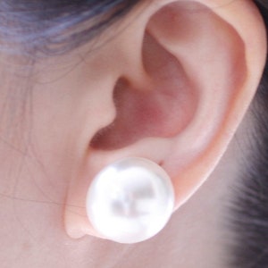May include: A white pearl earring stud, worn in the ear of a person with dark hair.