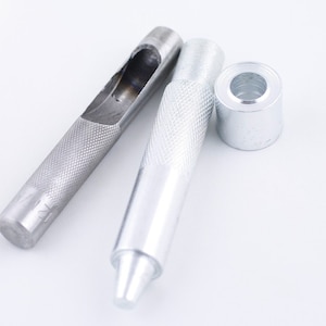 May include: Two silver metal leather hole punch tools and a silver metal grommet. The tools have a textured surface and the grommet is round.
