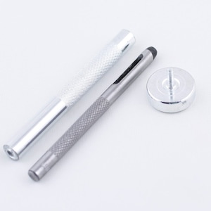 May include: A set of three silver metal tools for leather crafting. The tools include a punch, a hammer, and a base.