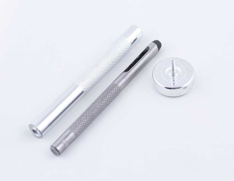 May include: A set of three silver metal tools for leather crafting. The tools include a punch, a hammer, and a base.