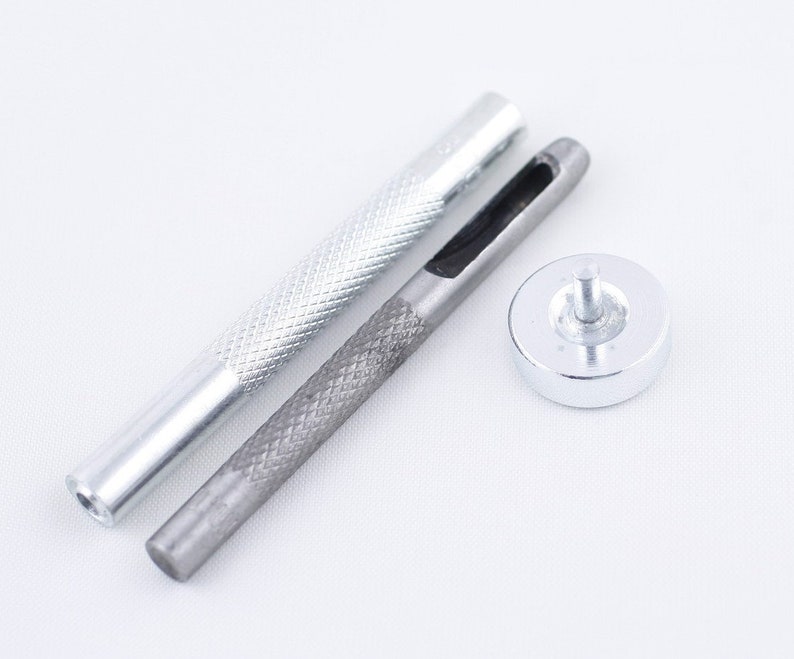 May include: A set of three silver metal tools for leather crafting. The tools include a punch, a hammer, and a handle.
