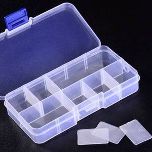 K&ouml;nnte beinhalten: Eine transparente Plastik-Aufbewahrungsbox mit einem blauen Verschluss. Die Box hat sechs F&auml;cher und ist ge&ouml;ffnet, um die F&auml;cher zu zeigen. Neben der Box befinden sich f&uuml;nf transparente Plastik-Teiler auf der schwarzen Oberfl&auml;che.