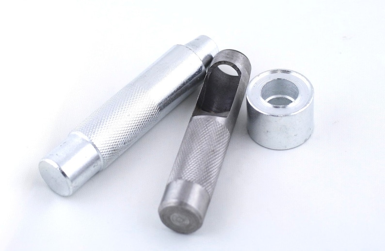 May include: A set of three silver metal tools for punching holes in leather. The tools include a punch, a hollow punch, and a setting tool.