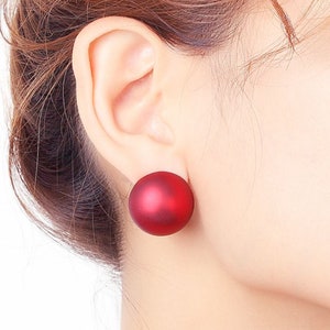 May include: A pair of red matte round stud earrings. The earrings are large and have a smooth, polished finish.