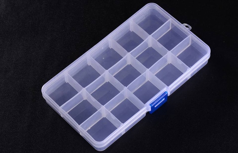 K&ouml;nnte beinhalten: Eine transparente Aufbewahrungsbox aus Kunststoff mit 12 F&auml;chern. Die Box hat einen blauen Verschluss an der Seite.