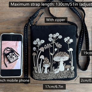 May include: A black fabric crossbody bag featuring white and brown embroidered mushrooms and wildflowers. The bag includes a zipper, an adjustable strap with a maximum length of 51 inches, and measures 7.5 inches by 6.7 inches by 0.8 inches.