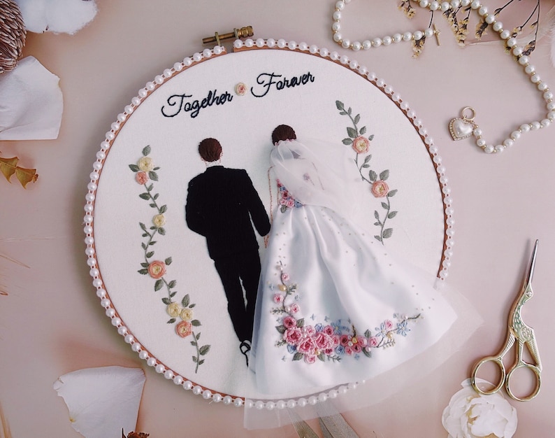 Pu&ograve; includere: Arte di ricamo a cerchio con una sposa e uno sposo in silhouette, con il testo "Together Forever" sopra di loro. Il cerchio &egrave; decorato con un bordo di perle e ricami floreali.