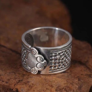 Puede incluir: Un anillo de plata con un dise&ntilde;o detallado que presenta un motivo floral y una banda texturizada.