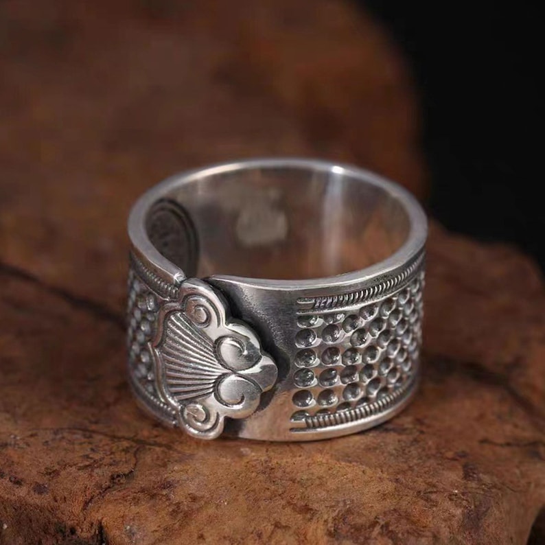 Puede incluir: Un anillo de plata con un dise&ntilde;o detallado que presenta un motivo floral y una banda texturizada.
