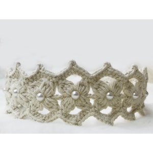 May include: A cream-colored crocheted headband with a delicate floral design and pearl accents.