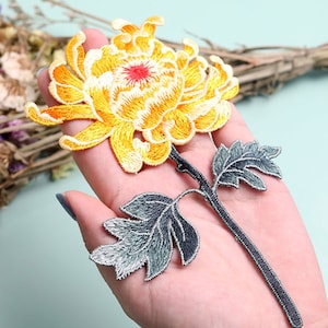 May include: A yellow embroidered flower with a gray stem and leaves. The flower is a chrysanthemum.