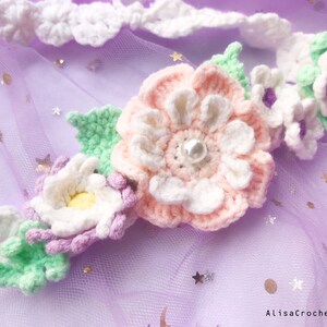 May include: A crocheted flower headband with pink, white, and green flowers. The headband is decorated with a pearl in the center of the largest flower.