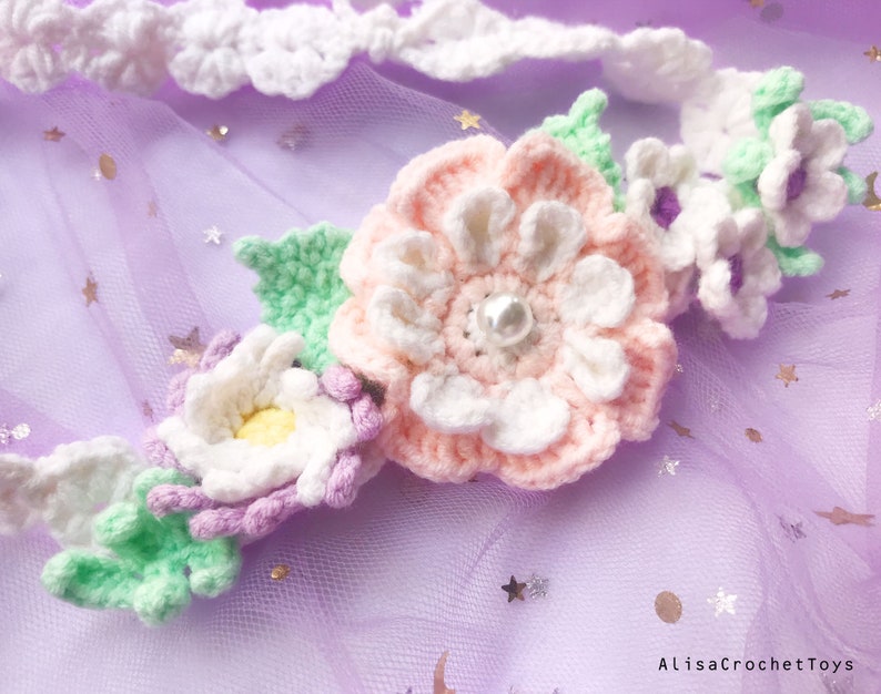 May include: A crocheted flower headband with pink, white, and green flowers. The headband is decorated with a pearl in the center of the largest flower.