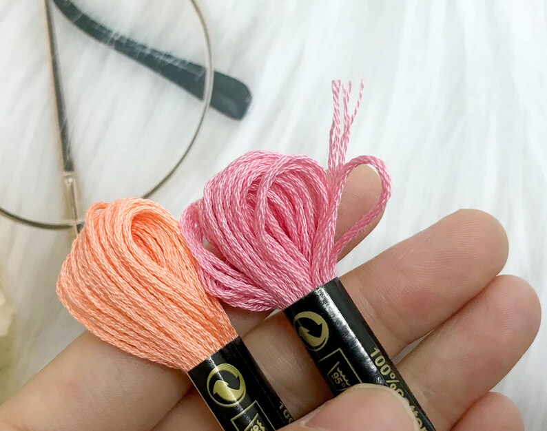 May include: Two spools of embroidery floss, one pink and one peach, with black labels that say "100% Cotton".