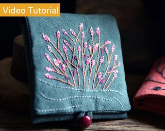 May include: A small teal blue fabric pouch with a floral embroidery design. The embroidery features pink and brown thread, depicting a cluster of branches with small pink flowers.