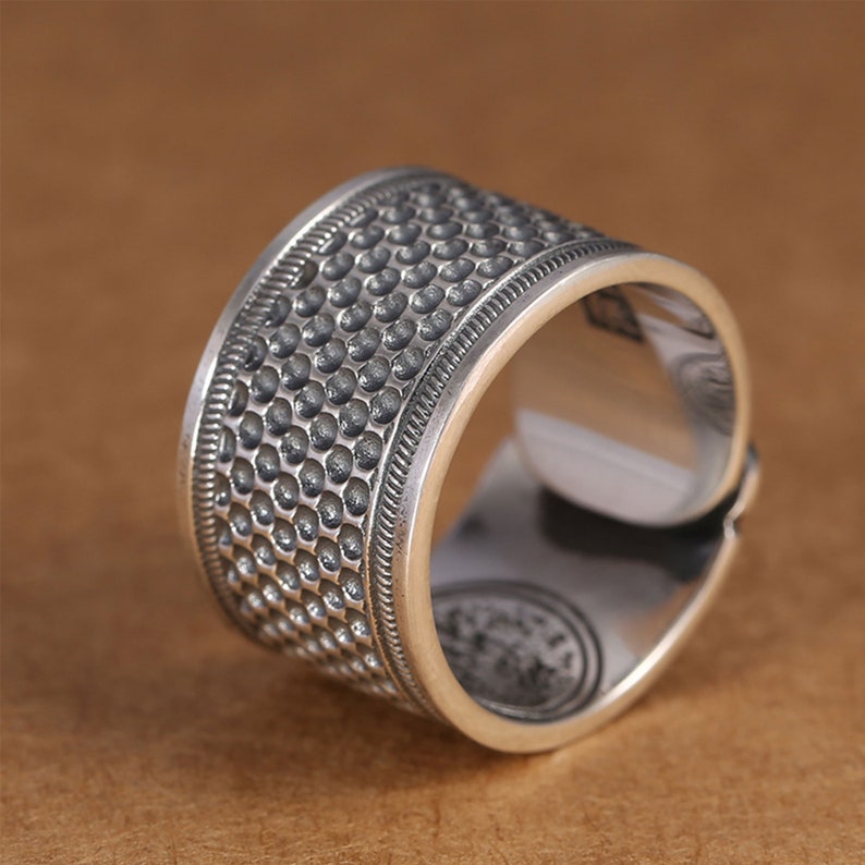 Puede incluir: Un anillo de plata con un acabado texturizado martillado. El anillo es ancho y tiene una banda redondeada.
