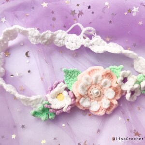 May include: A white crocheted headband with a floral design. The flowers are pink, white, and green. The headband is on a purple background.