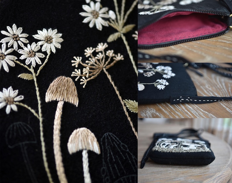 May include: A black crossbody bag featuring detailed embroidery of white daisies and tan mushrooms. The bag has a dark pink interior lining, a black zipper closure, and a thin black strap with white decorative stitching along the edges.