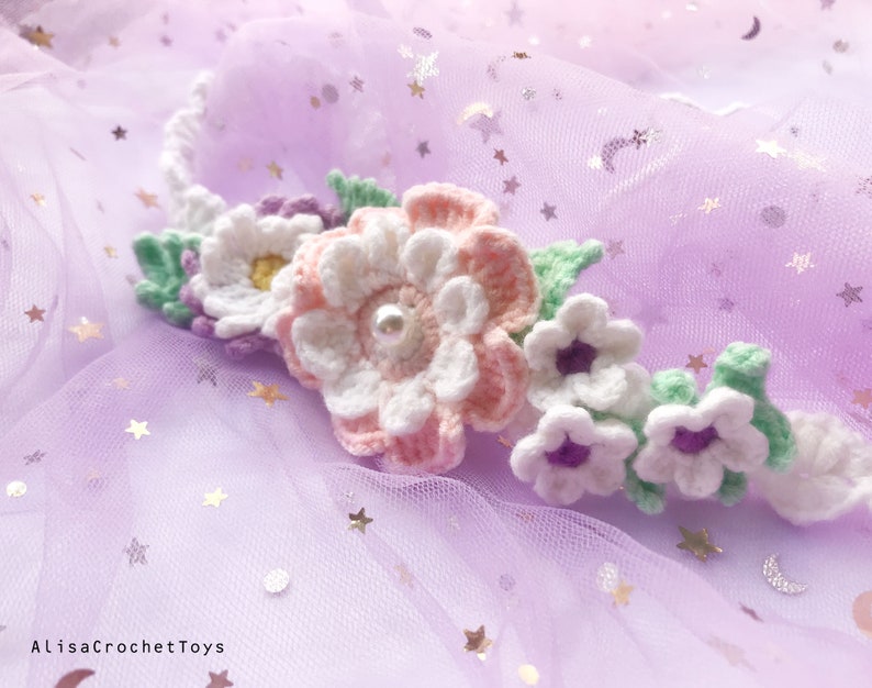 May include: A crocheted flower crown with white, pink, and purple flowers and green leaves. The crown is on a purple background with silver glitter stars.