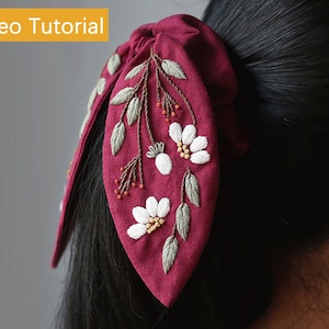 May include: A burgundy fabric hair scrunchie with embroidered white flowers and green leaves.
