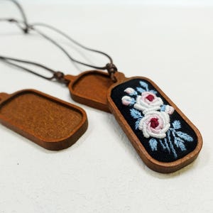 Pu&ograve; includere: Collane con ciondoli in legno con disegni floreali ricamati. I ciondoli hanno una cornice in legno scuro e un centro in tessuto nero. Il ricamo presenta rose rosa e bianche con foglie blu. Le collane hanno cordini marroni.