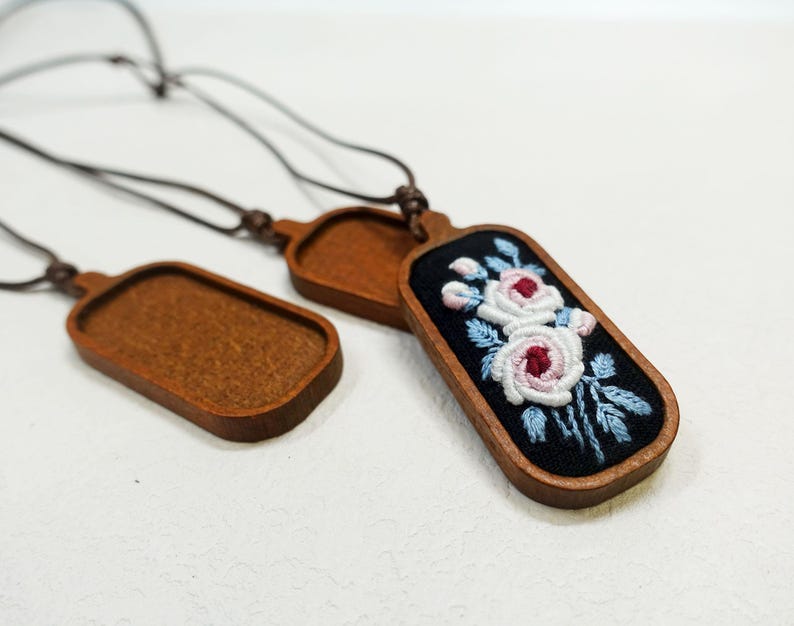 Pu&ograve; includere: Collane con ciondoli in legno con disegni floreali ricamati. I ciondoli hanno una cornice in legno scuro e un centro in tessuto nero. Il ricamo presenta rose rosa e bianche con foglie blu. Le collane hanno cordini marroni.