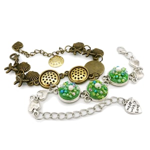 May include: Two bracelets with a silver chain and green beaded charms. One bracelet has a bronze chain with seashell and starfish charms. The charm on the silver bracelet says "made with love".
