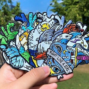 Puede incluir: Un conjunto de parches bordados de colores para planchar que representan un corazón con varios diseños, entre ellos una mariposa, una ola y un rayo. Los parches tienen un estilo caprichoso y abstracto. Un parche tiene el texto "Fight Like A Girl".