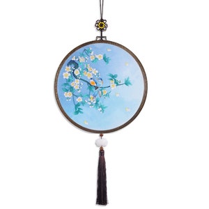 May include: A round, blue and white embroidered wall hanging with a floral design and two birds. The hanging has a black tassel and a small, white bead.