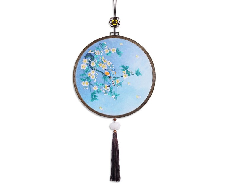 May include: A round, blue and white embroidered wall hanging with a floral design and two birds. The hanging has a black tassel and a small, white bead.