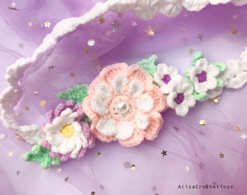 May include: A crocheted flower headband with pink, white, and green flowers. The headband is on a purple background with silver glitter stars.