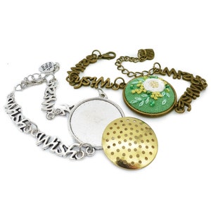 May include: Two silver charm bracelets with the word "Wish" repeated on each. One bracelet has a blank round charm and the other has a green embroidered charm with a white flower and yellow leaves. A gold charm with a circular pattern is also included.