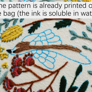 Puede incluir: Primer plano de una tela blanca con un p&aacute;jaro azul, una rama marr&oacute;n y hojas verdes y amarillas bordadas sobre ella. El texto "The pattern is already printed on the bag (the ink is soluble in water)" es visible en la parte superior de la imagen.