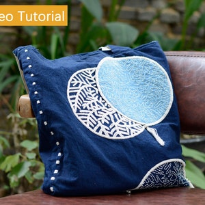 Könnte beinhalten: Eine marineblaue Tragetasche mit weiß gestickten Fächer- und Blattmotiven. Die Tasche hat weiße Nähte an den Kanten und den Text "Video Tutorial" in einem gelben Feld oben links.