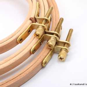 May include: Three wooden embroidery hoops with brass screw-on tightening mechanisms. The hoops are nested together, with the largest hoop on the bottom and the smallest hoop on top.