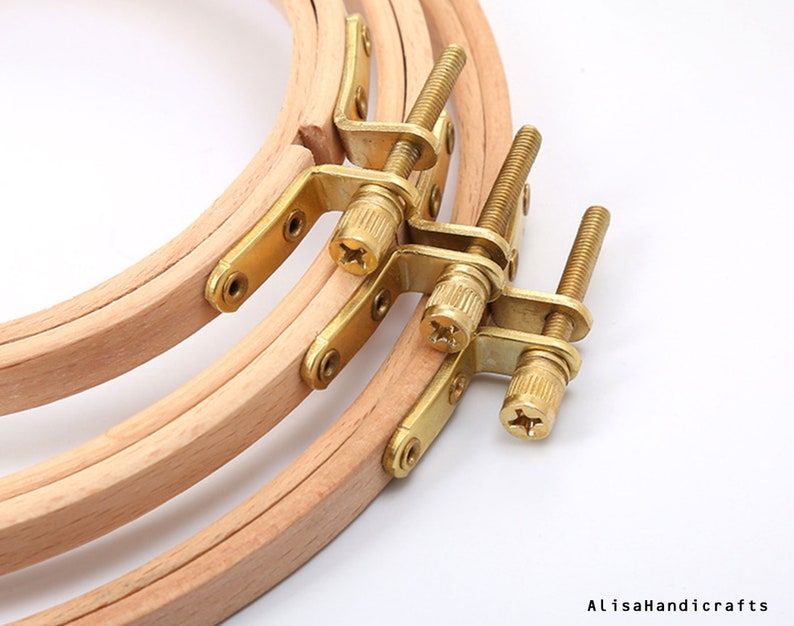 May include: Three wooden embroidery hoops with brass screw-on tightening mechanisms. The hoops are nested together, with the largest hoop on the bottom and the smallest hoop on top.