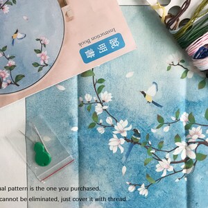 May include: A close-up of a needlepoint embroidery kit featuring a blue and white floral design with birds. The kit includes a pre-printed canvas, embroidery floss, needles, and instructions. The actual pattern is the one you purchased. The ink cannot be eliminated, just cover it with thread.